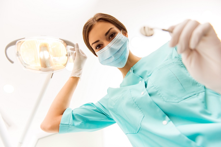Young woman dentist in protection gloves and a mask, keeps dental instrument looking at the camera.